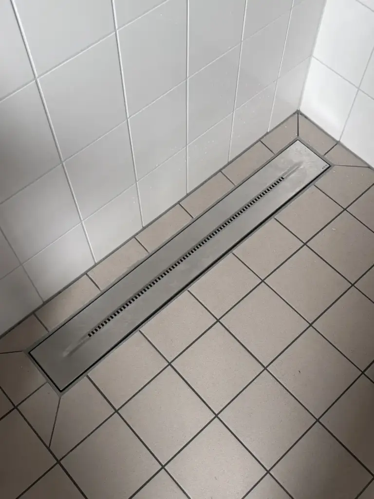 Afgewerkte rvs-douchegoot langs de wand in een betegelde douchevloer.