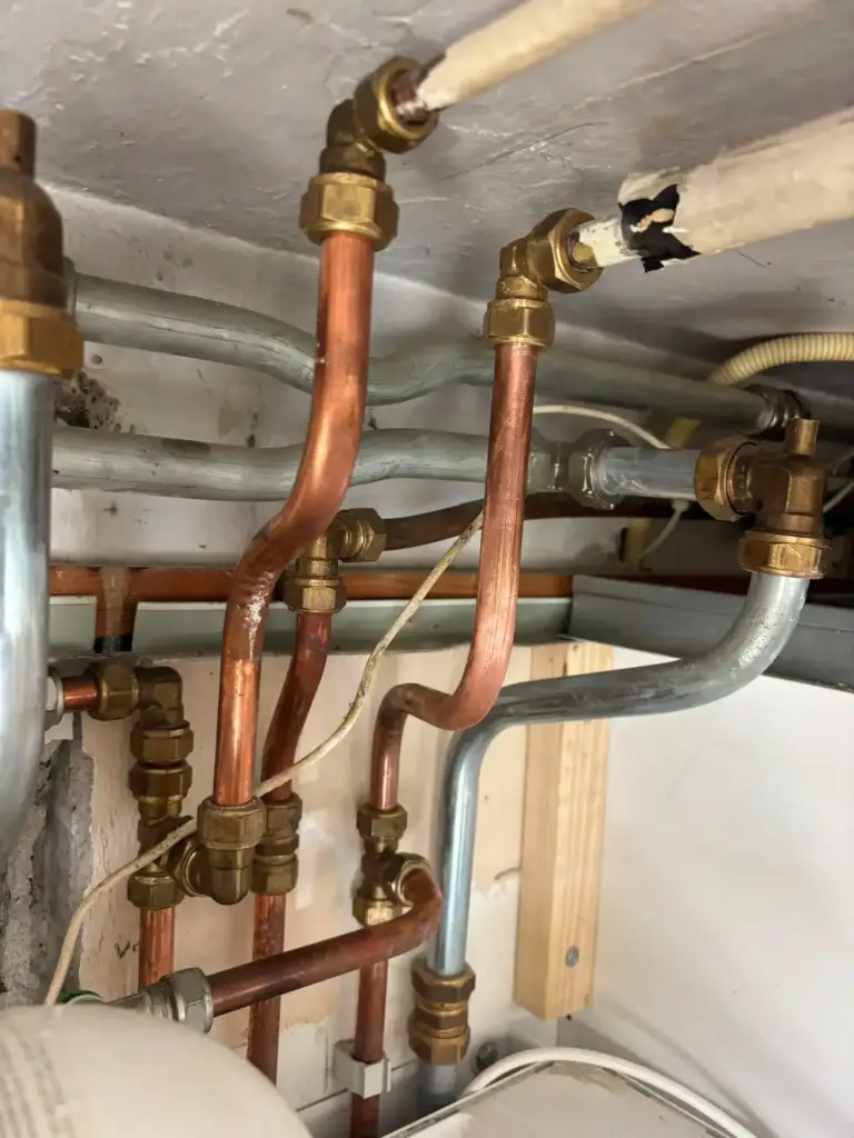 Nieuw aangelegde koperen leidingen met knelkoppelingen onder een plafond.