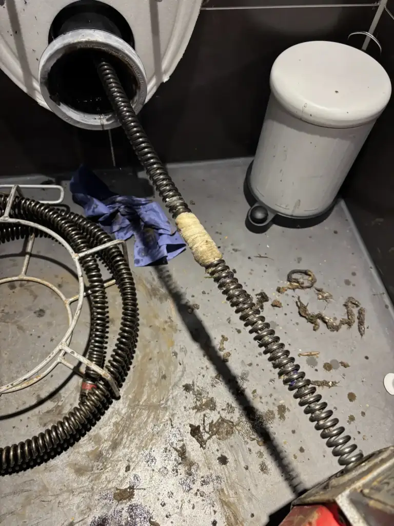 Ontstoppingsveer van een trommelmachine in een toiletafvoer.